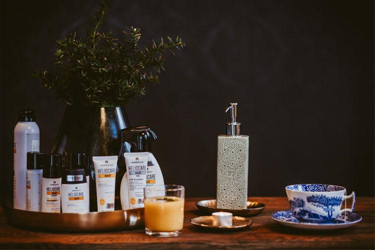 Et bord med hudpleieprodukter, en glass med juice, og en kopp med fat i blått og hvitt.
