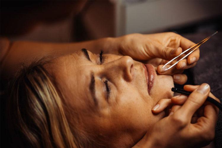 Kvinne får kosmetisk behandling med pinsett og eyeliner i en skjønnhetssalong.