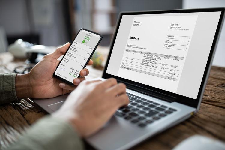 En person som bruker en laptop og en mobiltelefon for å se på en faktura.