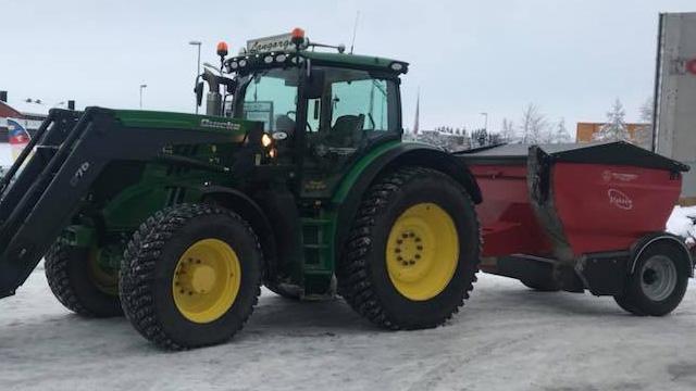 Grønn traktor med gule dekk som trekker en rød tilhenger på snødekt vei.