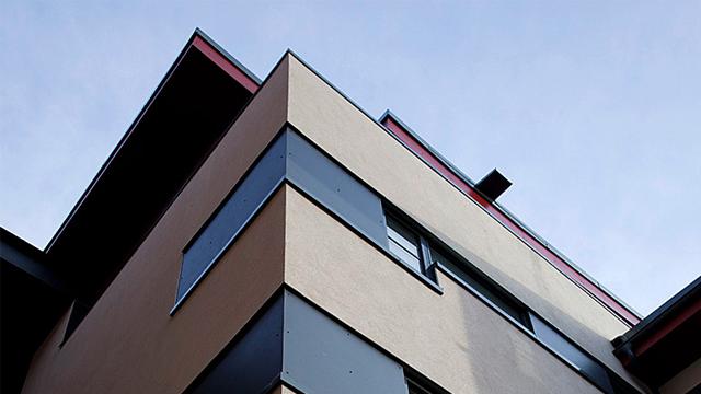 Moderne bygning med store vinduer og en unik fasade, sett fra bakkenivå mot himmelen.