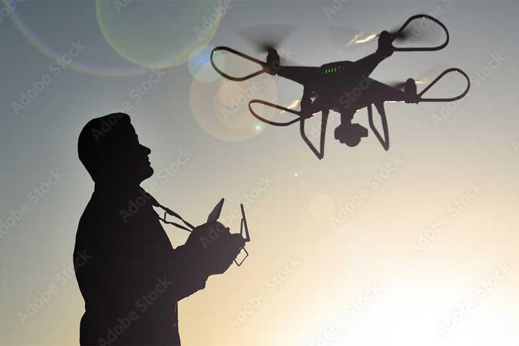 Mann som styrer en drone med fjernkontroll mot en solfylt bakgrunn.
