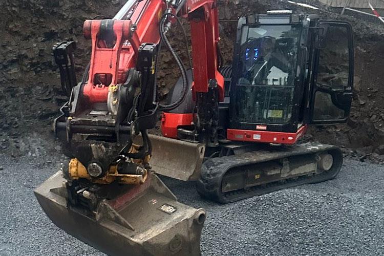 Gravemaskin med skuffe som arbeider på en byggeplass med grusunderlag.