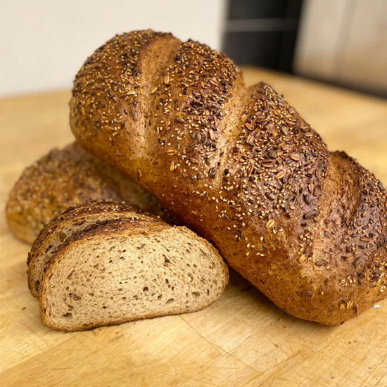 Nystekt brød med frø, plassert på en treskjærefjøl, med en skive skåret av brødet.