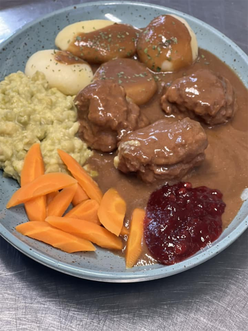 En tallerken med kjøttkaker i brun saus, poteter, ertestuing, gulrøtter og tyttebærsyltetøy.