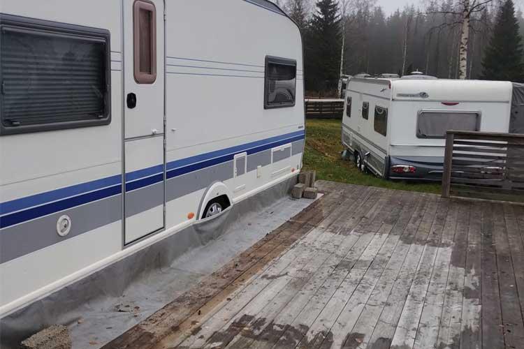 To campingvogner parkert på en tredekk, med skog i bakgrunnen.