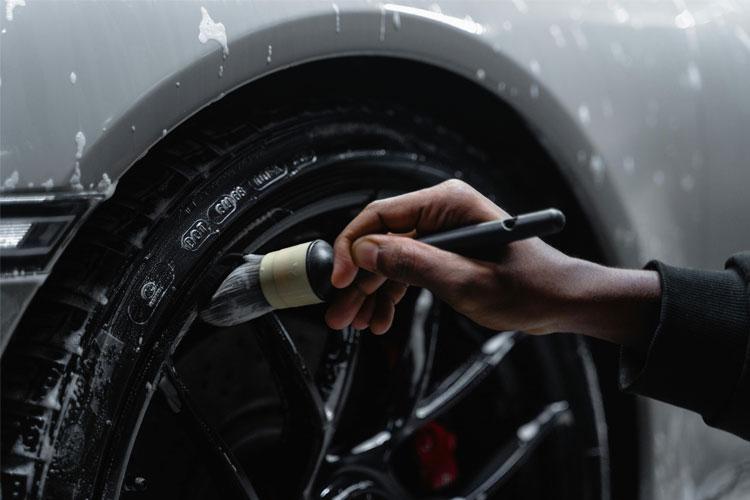 En person rengjør dekkene på en bil med en børste og såpe, mens bilen står på en vaskeplass.