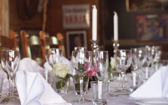 Et elegant dekket bord med glass, servietter og blomster i en koselig restaurant.