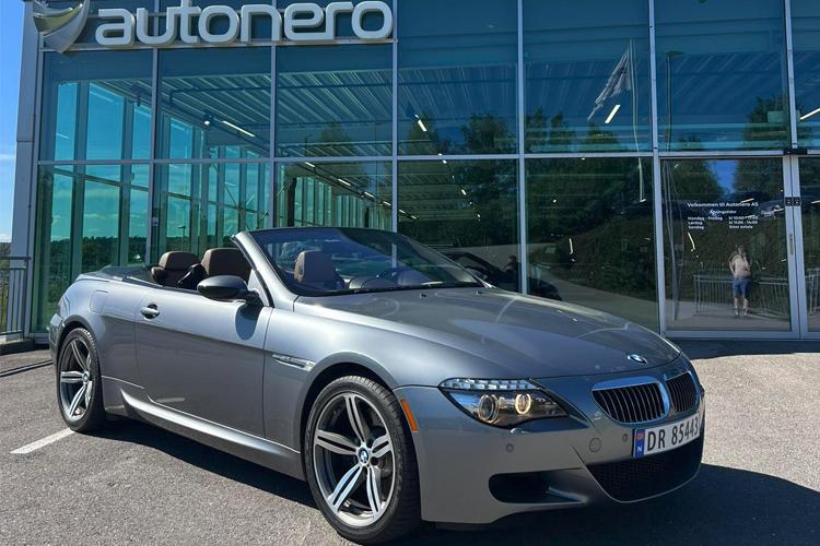 Grå BMW kabriolet parkert foran Autonero bygning med glassfasade.