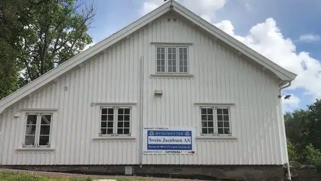 Hvit trebygning med flere vinduer og et skilt som viser navnet på firmaet Svein Jansen AS.