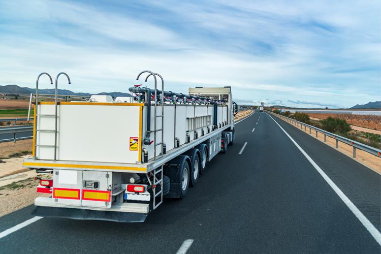 En lastebil med tank på motorveien, omgitt av landskap og blå himmel.