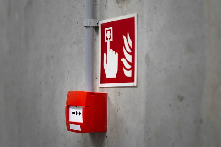 Rød brannalarm med en hånd som peker på en brannvarselsymbol på en grå vegg.