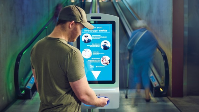 En mann står foran en digital informasjonsskjerm i en undergrunnsstasjon, med rulletrappen i bakgrunnen.