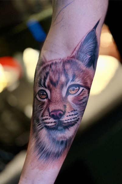 Tatovering av en gaupe med detaljerte ansiktstrekk på en arm.