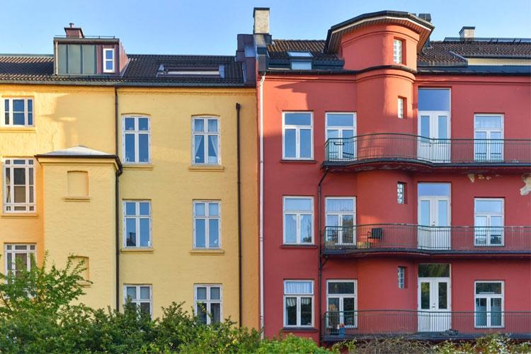 Fargerike leilighetsbygg i gult og rødt med balkonger og vinduer i sollys.