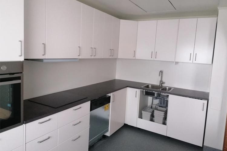 Moderne kjøkken med hvite skap, svart benkeplate og oppvaskmaskin under benken.