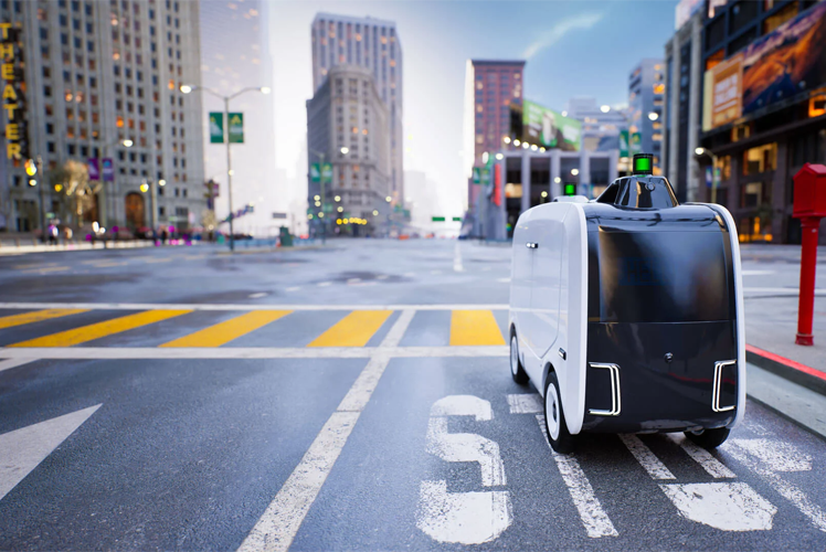 En autonom leveringsrobot står på en gate i en by med høye bygninger i bakgrunnen.
