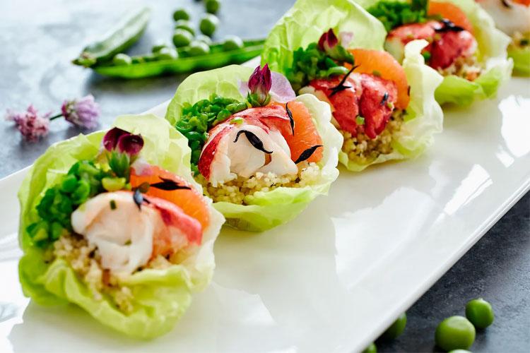 Friske salatblader fylt med reker, laks og quinoa, dekorert med blomster og grønnsaker på en hvit tallerken.