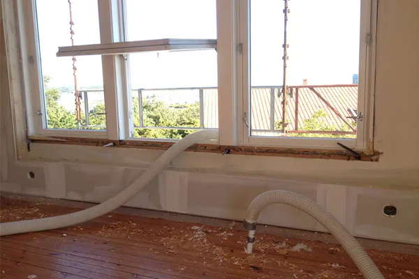 Renovering av rom med vinduer, rør som fører ut, og treverk på gulvet. Utsikt til hagen utenfor.