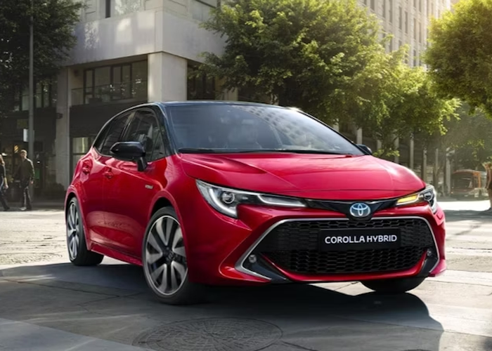 Rød Toyota Corolla Hybrid parkert på en gate med moderne bygninger i bakgrunnen.