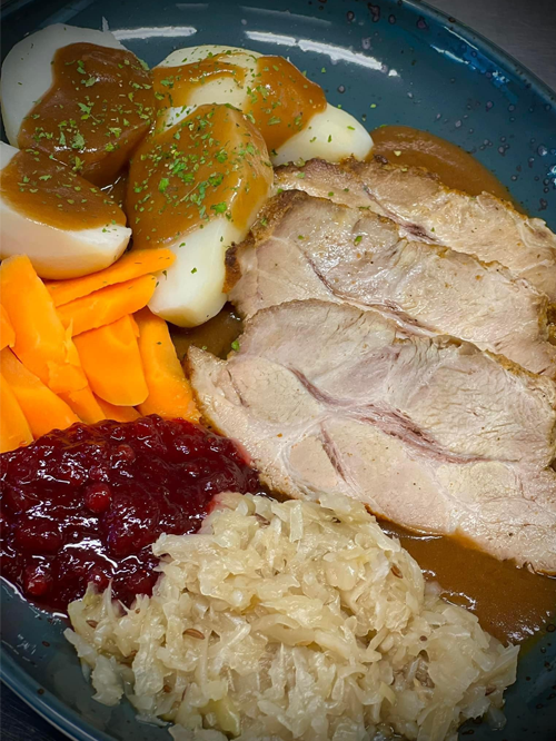En tallerken med kokt svinekjøtt, poteter, gulrøtter, rødkål og brun saus, dekorert med persille.