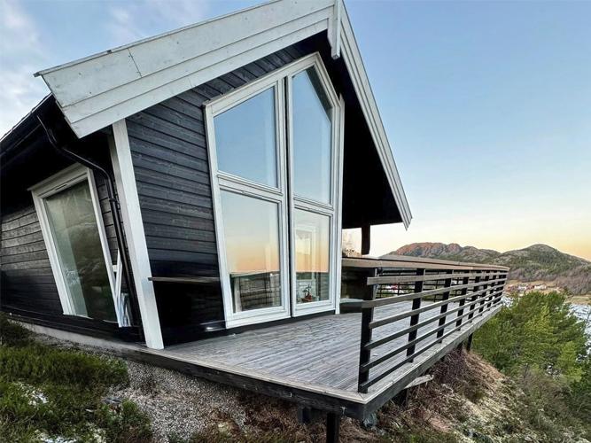 Moderne hytte med store vinduer og terrasse, beliggende på en fjellside med utsikt over landskapet.