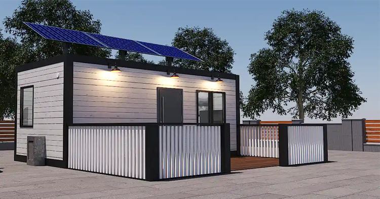 Moderne hus med solcellepaneler, terrasse og tretrapp, omgitt av trær under en klar himmel.