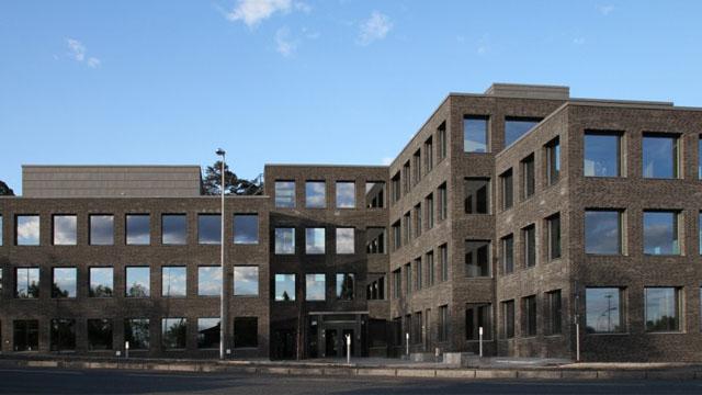Moderne kontorbygg med store vinduer og en mursteinsfasade, beliggende i et åpent område.