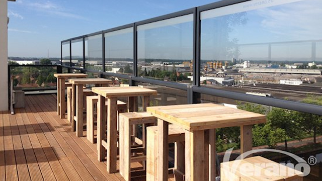 Utsikt fra en terrasse med tre barstoler og et moderne glassrekkverk.