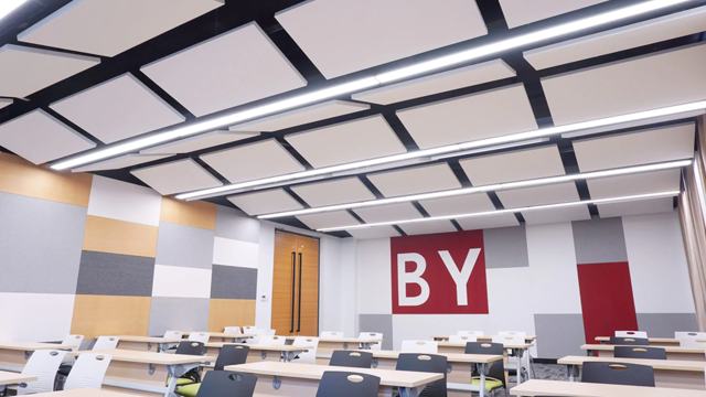 Moderne klasserom med lys tak, bord i rekke og en vegg med røde og grå paneler med teksten "BY".