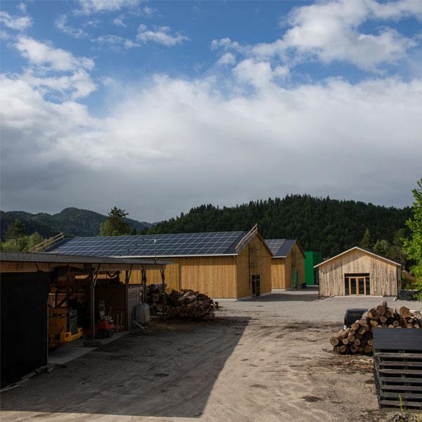 Moderne bygninger med solcellepaneler på taket, omgitt av fjell og trær i et landlig område.