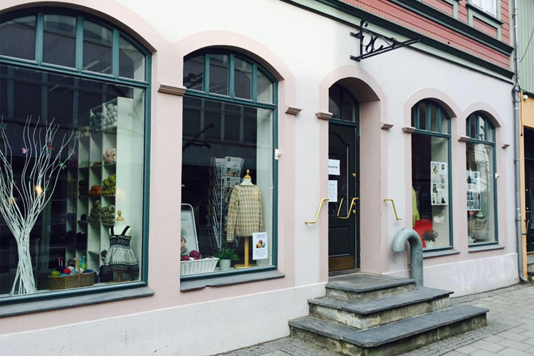 En butikkfasade med store vinduer, trapper og dekorative elementer, beliggende i en bygate.