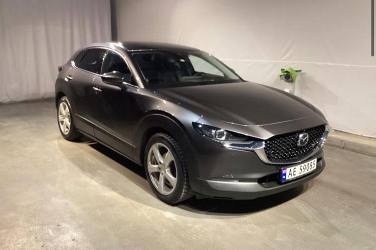 En grå Mazda CX-30 SUV parkert i et rom med hvite vegger og en ladestasjon.