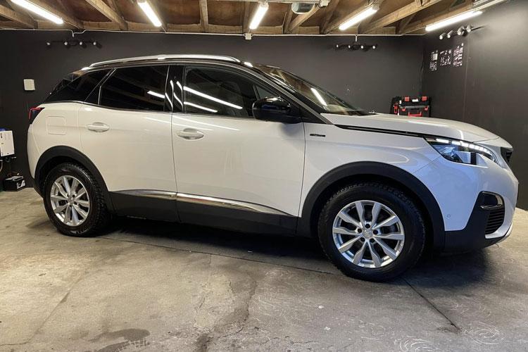 En hvit SUV parkert i et garasjeområde med mørke vegger og belysning.