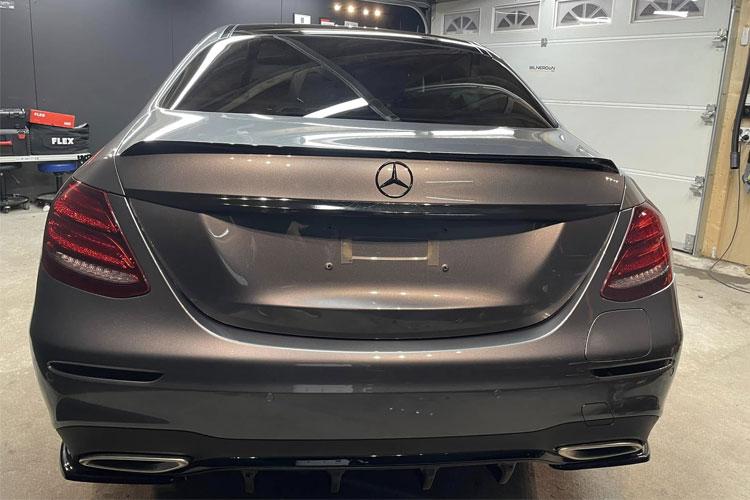 Bakpartiet av en grå Mercedes-Benz med sportslig design, stående i en garasje med verktøy i bakgrunnen.