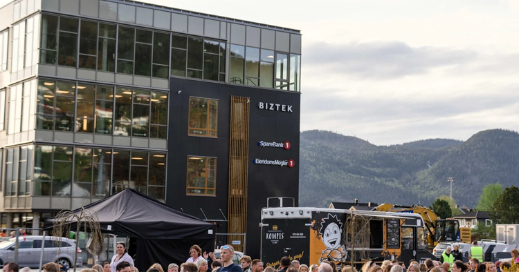 Folkemengde foran en moderne bygning med matvogn og fjell i bakgrunnen.