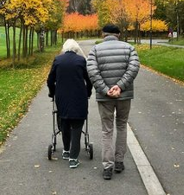 Eldre par går sammen på en sti i en park med høstfarger i trærne rundt dem.