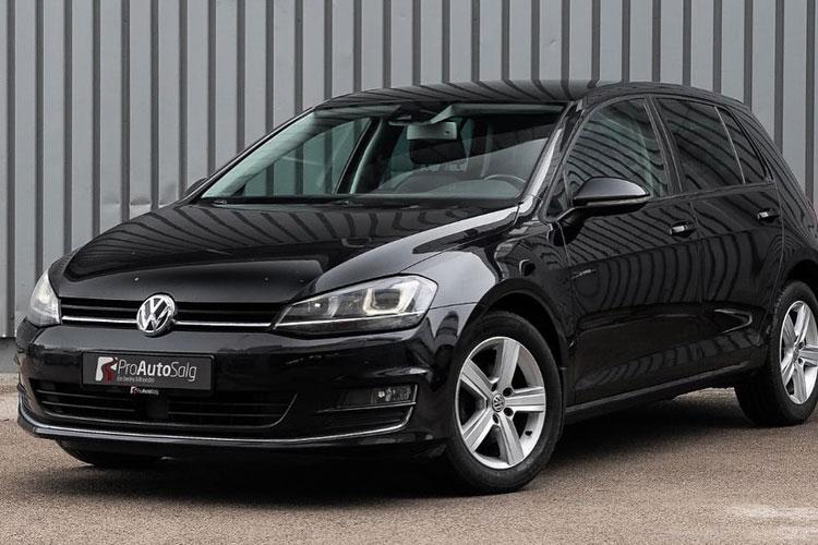 En svart Volkswagen Golf parkert foran en grå vegg med moderne linjer.