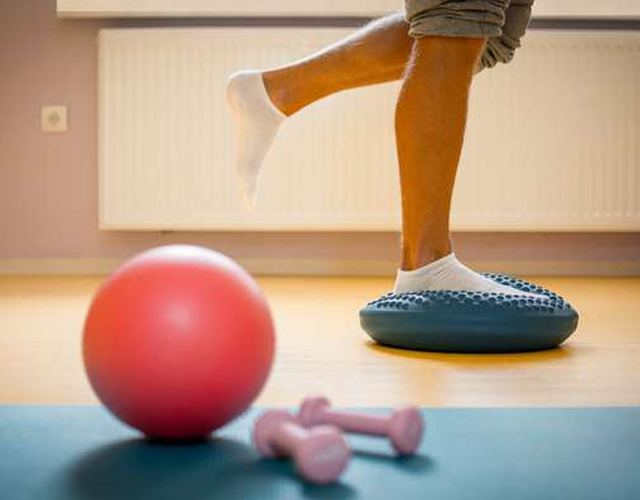 En person står på en balansepute med ett ben hevet, med en rosa ball og små manualer i forgrunnen.