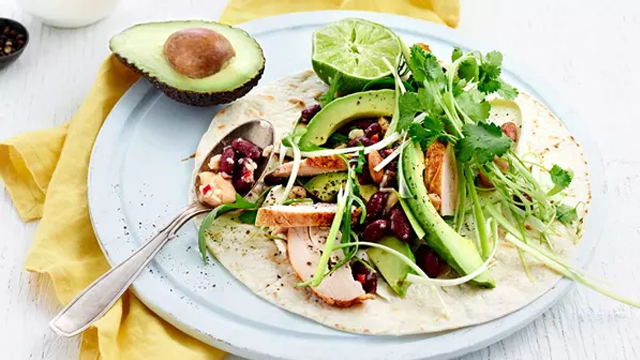 En tallerken med en tortilla fylt med kylling, avokado, lime, bønner og friske urter.