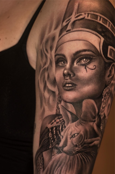 Detaljert tatovering av en kvinne med egyptisk inspirert design og en katt på armen.