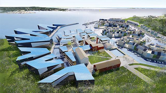 Oversiktsbilde av en moderne havn med bygninger og båter ved vannkanten, omgitt av grønt landskap.
