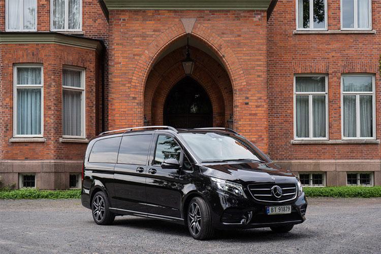 En svart Mercedes varebil parkert foran en rød murbygning med buet inngang.