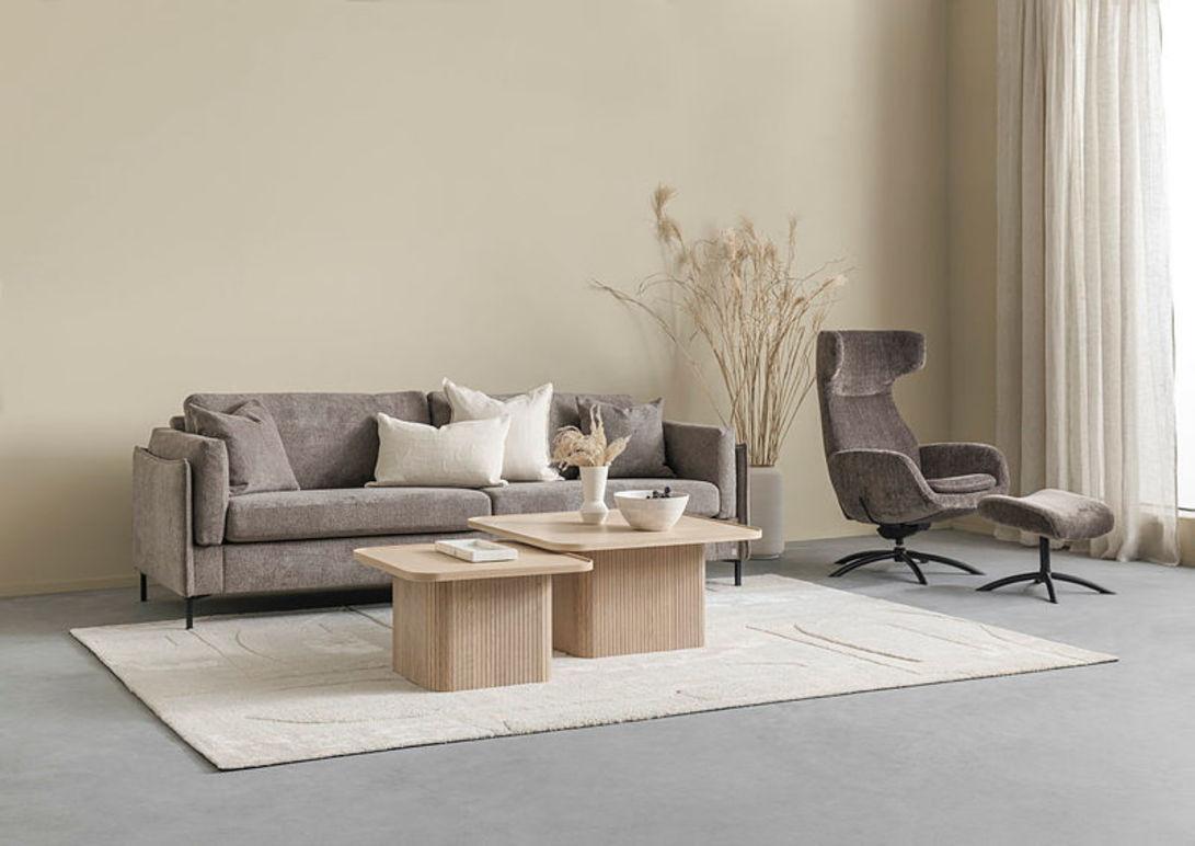 Moderne stue med grå sofa, to bord i tre, en lenestol og dekorative planter på et lyst teppe.
