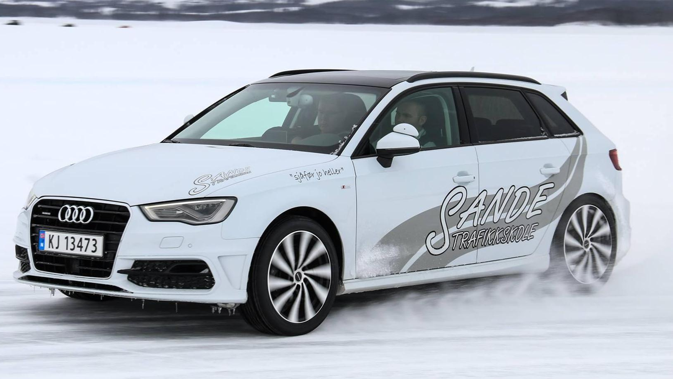 En hvit Audi A3 med Sande-klistremerker kjører på snøen, spruter snø rundt seg.