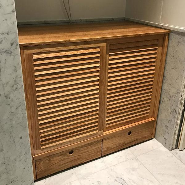 En moderne, tre-farget skap med louvered dører og to skuffer, plassert i et rom med marmorvegger.