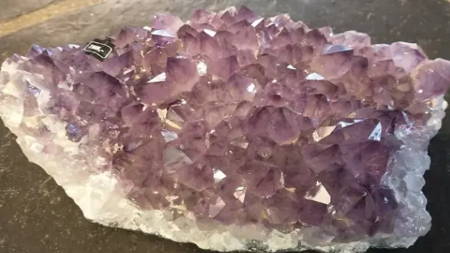 En stor amethystkrystall med lilla spisser, plassert på en mørk overflate.