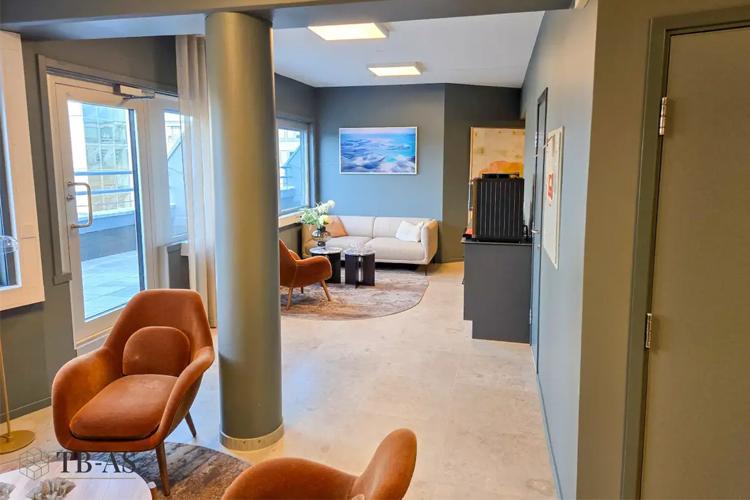 Moderne stue med sofa, stoler og kunstverk på veggen, store vinduer som slipper inn naturlig lys.