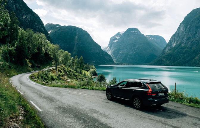 En svart SUV parkerer langs en vei med fjorder og fjell i bakgrunnen.