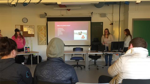 Studenter presenterer i et klasserom med datamaskiner og en projektor som viser en presentasjon.